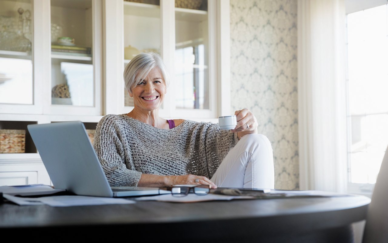 Kvinne sitter ved bord med pc og kaffe